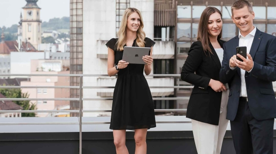 Zwei Frauen und ein Mann mit jeweils einem Handy und Tablet in der Hand