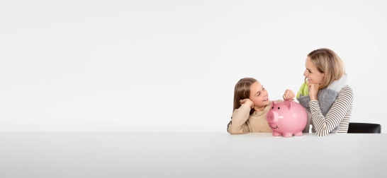 Frau und Kind schauen sich lächelnd an. In ihrer Mitte steht ein pinkes Sparschwein.