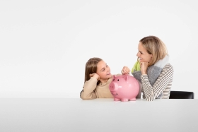 Frau und Kind schauen sich lächelnd an. In ihrer Mitte steht ein pinkes Sparschwein.