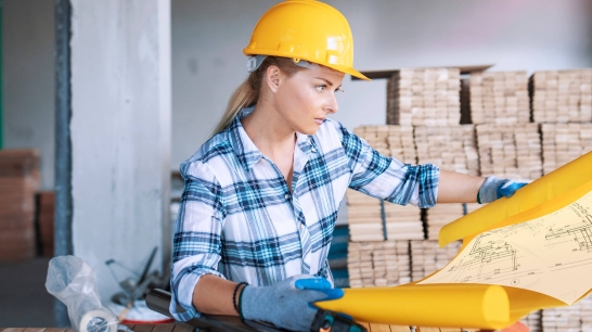 Frau mit gelben Helm auf Baustelle liest Bauplan